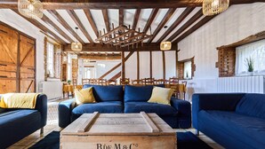 A rustic interior with exposed wooden beams, a blue sofa set, and a vintage wooden chest labeled 'Bde M&C 2ME SEMESTRE 1939'. - Gîte 14 people - 5 bedrooms - 5 bathrooms - Large spaces (Fontaine-sur-Ay)