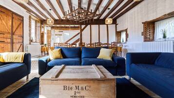 Un intérieur rustique avec des poutres apparentes, un canapé bleu et une vieille malle en bois portant l’inscription « Bde M&C 2e semestre 1939 ».