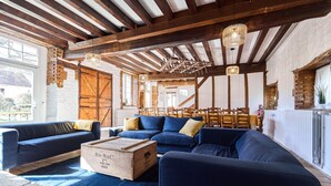 A rustic interior with exposed wooden beams, a blue sectional sofa, and a wooden chest labeled 'BéM & Co. 2ème SEMESTRE 1939'. - Gîte 14 people - 5 bedrooms - 5 bathrooms - Large spaces (Fontaine-sur-Ay)