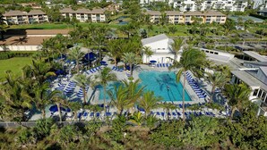 An aerial view of a resort with a central swimming pool surrounded by lounge chairs and palm trees. - OV 916 Golf Course View Condo - Welcome to Paradise (Fort Pierce)