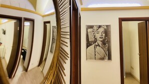 A hallway with a large mirror, a framed black and white portrait, and wooden doors.