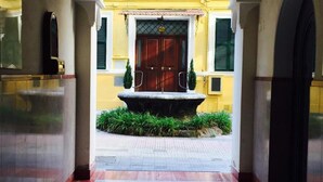 A corridor with a fountain, a yellow building, and a wooden door.