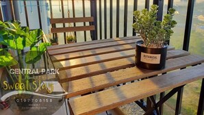 Ein Holztisch mit einem Blumentopf, beschriftet mit 'BOTANICAL', auf einem Balkon mit Blick auf die Stadt.