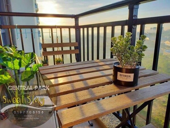 Ein Holztisch mit einem Blumentopf, beschriftet mit 'BOTANICAL', auf einem Balkon mit Blick auf die Stadt.