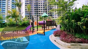 Ein Spielplatz mit Rutschen und einer Kletterkonstruktion, umgeben von Grünflächen und einem blauen Spielbereich, mit hohen Gebäuden im Hintergrund.