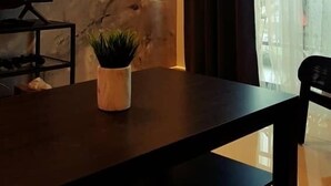 Ein modernes Wohnzimmer mit dunklem Holzpaneel, einem Flachbildfernseher auf einem Standfuß, einer Topfpflanze und einem großen Fenster mit Vorhängen.