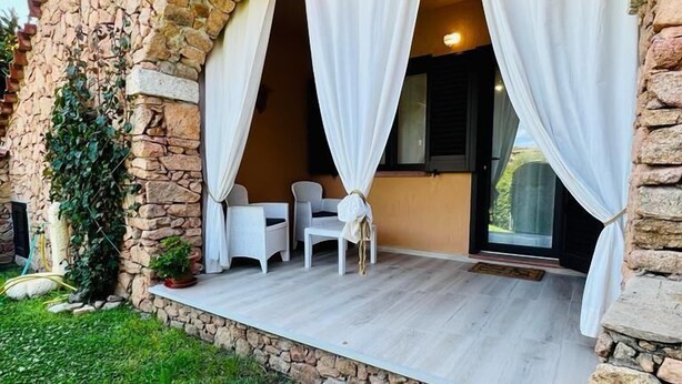 A stone building with a covered patio area featuring two white chairs and a small table. - Residence Oasi La Cinta Centro (San Teodoro)