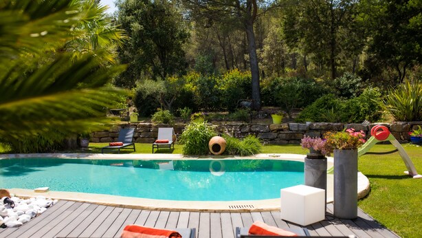 Una piscina con maderas, sillas de descanso y un muro de piedra con vegetación.