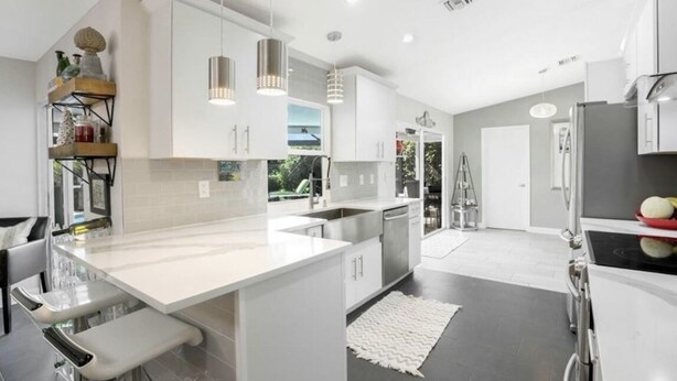 A modern kitchen with white cabinetry, stainless steel appliances, and pendant lighting. - Four Bedroom Pool Home close to Beach (Naples)