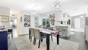 A modern kitchen with a dining area, featuring a chandelier, white cabinetry, and a large island. - Four Bedroom Pool Home close to Beach (Naples)