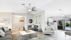 A modern living room with a grey sofa, a white coffee table, and a grey armchair. There is a ceiling fan, a large globe decoration, and a small side table with a plant. - Four Bedroom Pool Home close to Beach (Naples)