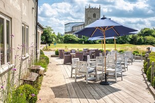 An outdoor patio with white chairs and a large umbrella, a stone building with scaffolding in the background, and a church tower.