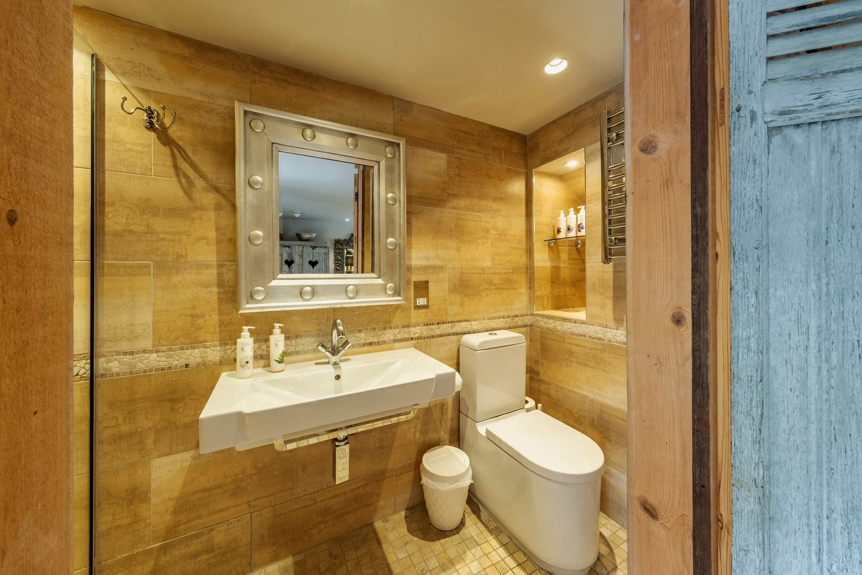 Un baño con tocador, lavamanos, espejo con luces, inodoro y un cubo de basura.
