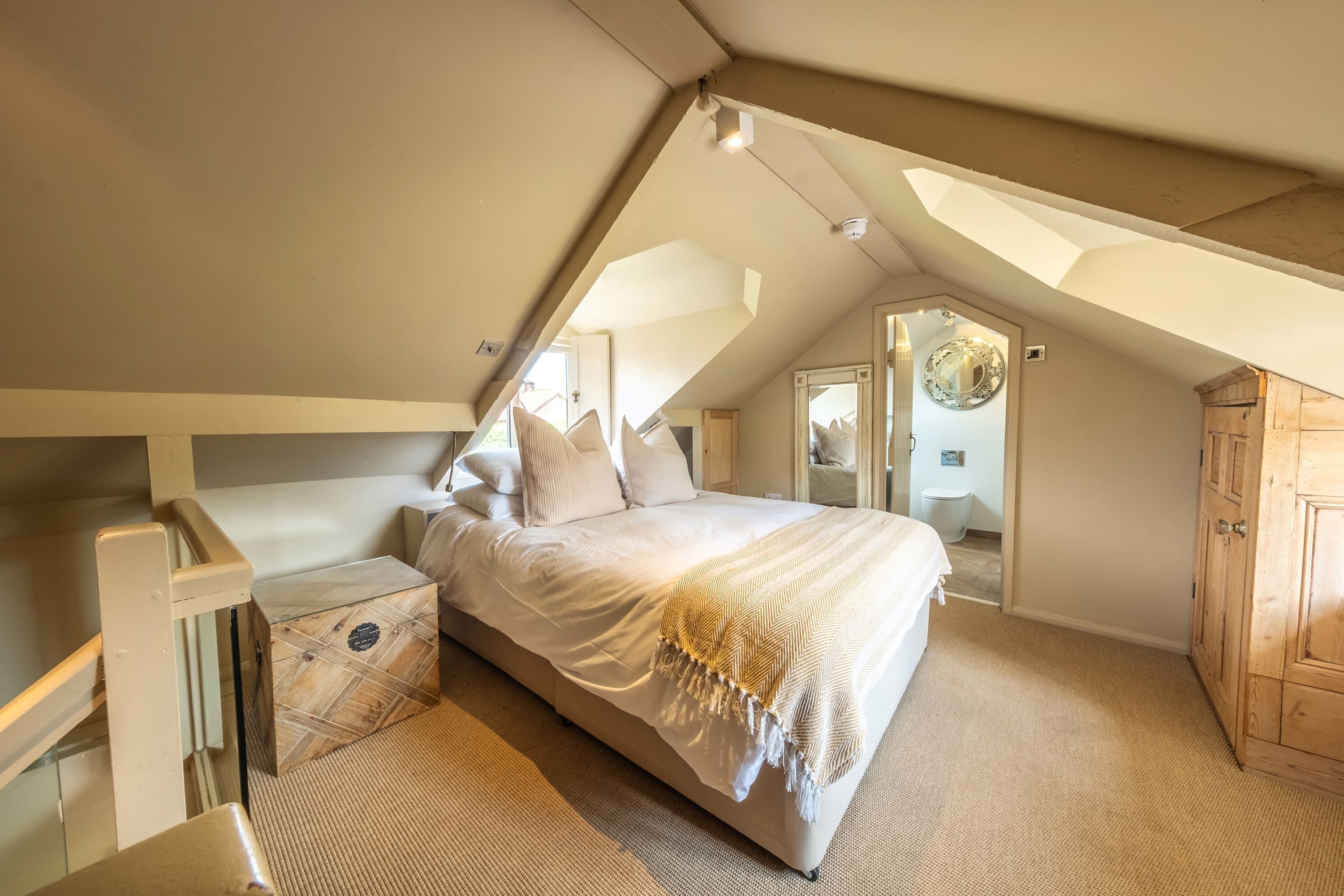 A bedroom with a sloped ceiling, a bed with white bedding, a wooden chest of drawers, and a mirror on the wall.