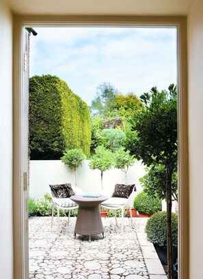Relax in a serene garden setting with a patio featuring a circular table and two cushioned chairs.
