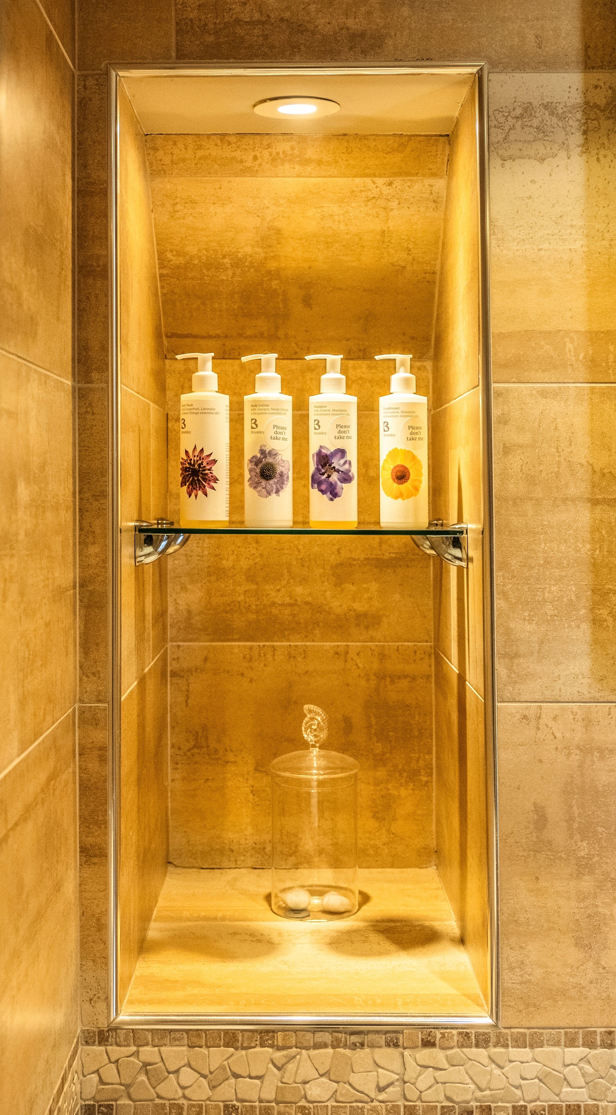 Une douche avec une porte en verre, une étagère pour les articles de toilette et un sol carrelé en pierre.