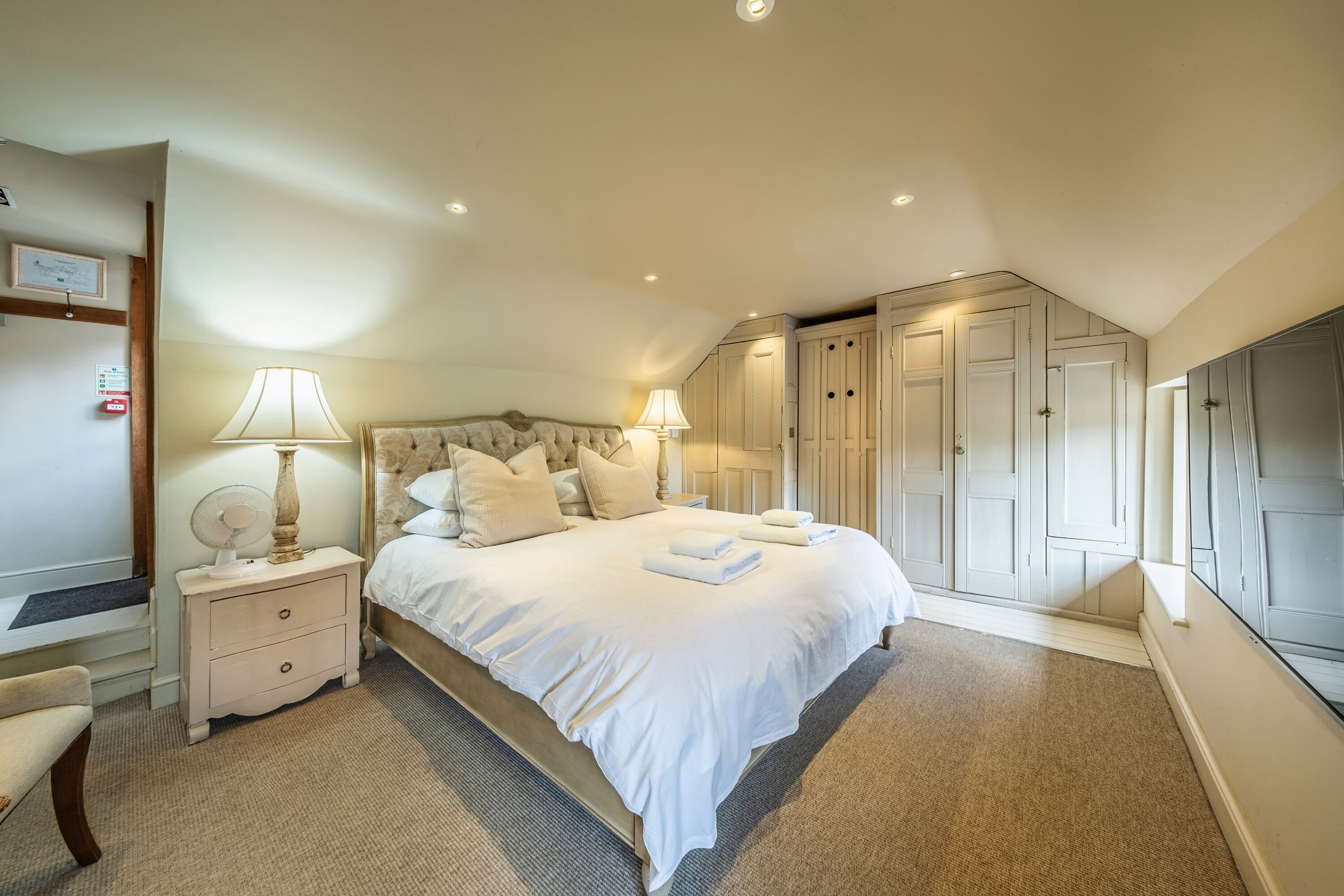 A bedroom with a large bed, two bedside tables with lamps, a chair, and a wardrobe.