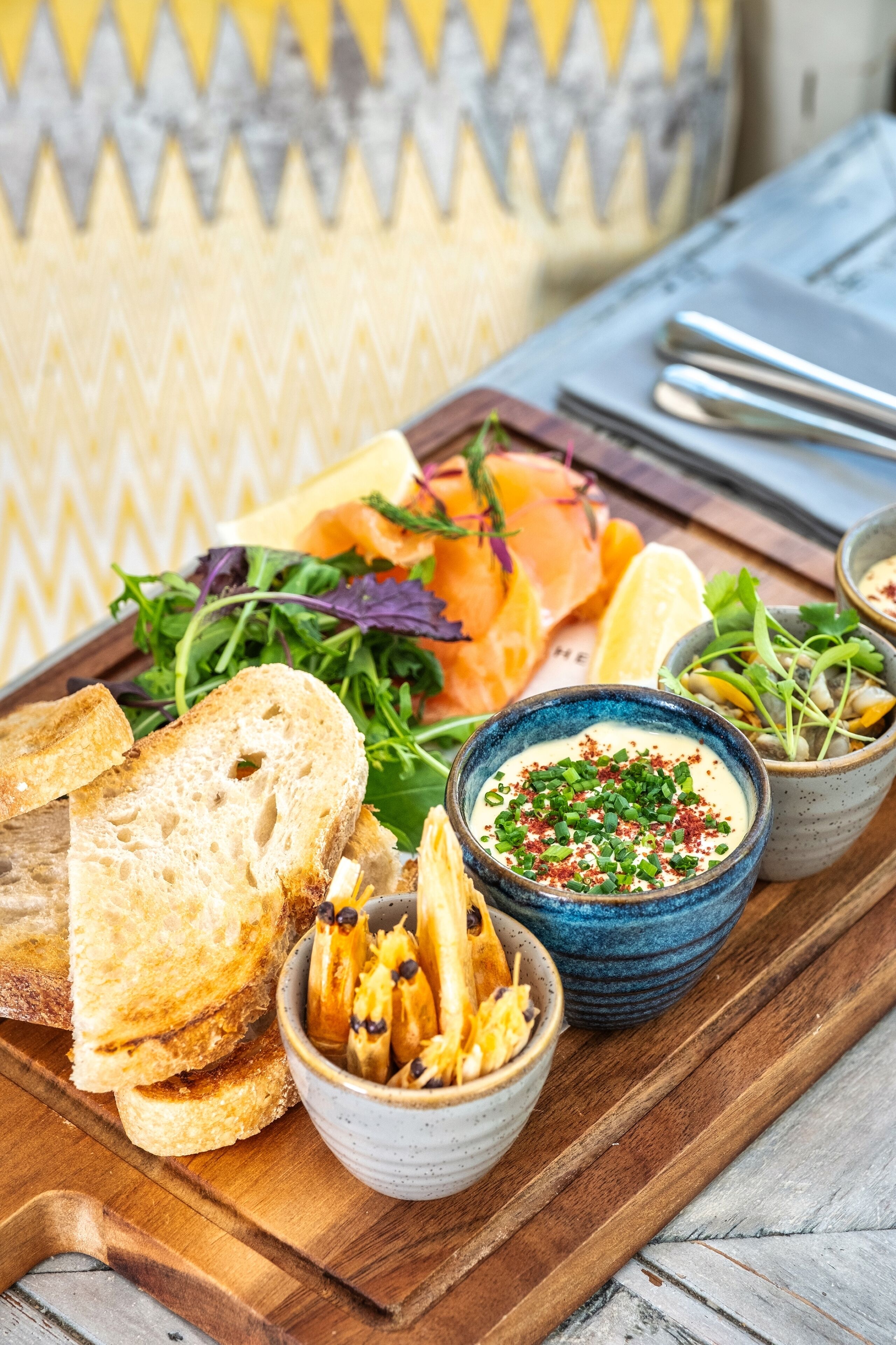 A wooden board with various food items including bread, salad, and bowls of dips.