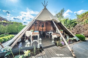 Una tienda tipo tipi con una terraza de madera, mobiliario exterior y plantas en macetas.