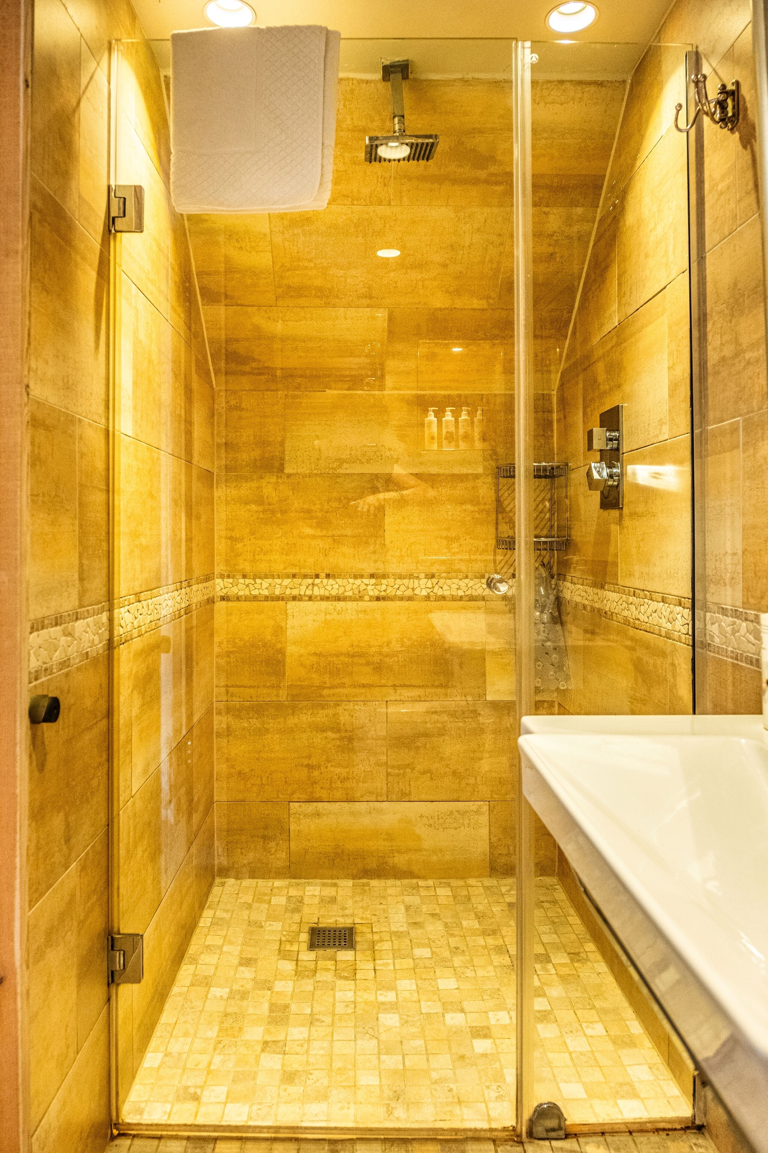 Une douche fermée par des parois de verre, avec un sol carrelé et une serviette blanche accrochée au mur.
