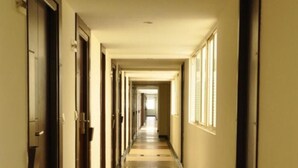 A long, narrow hallway with doors on both sides and windows on the right wall. - Hotel Shaans (Tiruchirappalli)