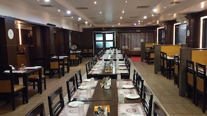 A restaurant with long communal tables, individual booths, and a high ceiling with recessed lighting. - Hotel Shaans (Tiruchirappalli)