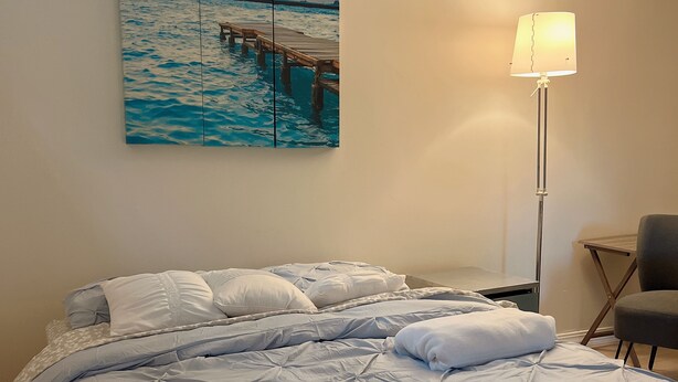 A hotel room with a bed, a desk, a chair, and a painting of a sunset over the ocean. - Private, Clean and Charming at amazing rate (Manchester)