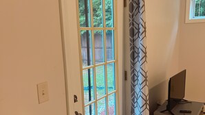 A room with a door leading to a backyard, a desk with a computer, and a patterned curtain. - Private, Clean and Charming at amazing rate (Manchester)