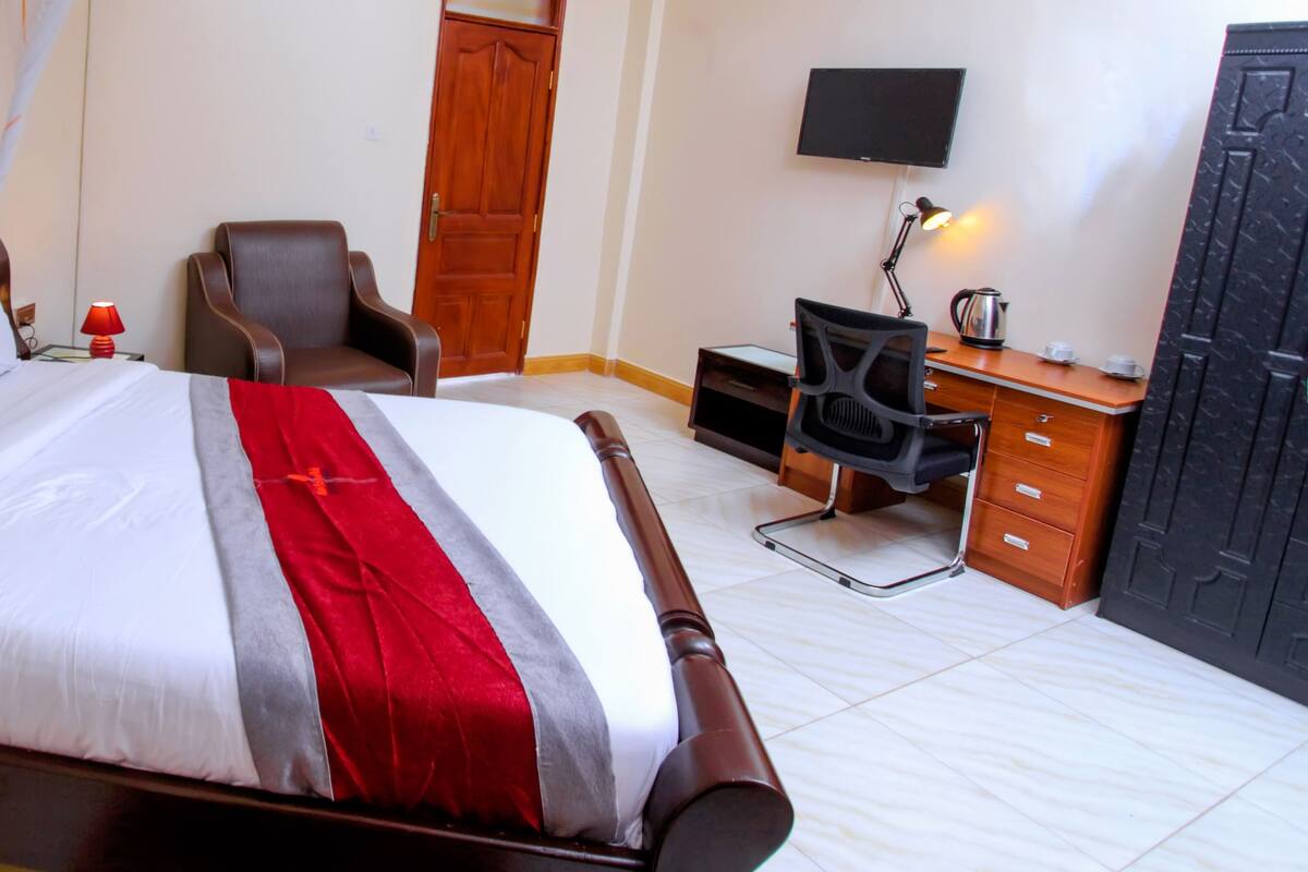 A hotel room with a bed, a desk, a chair, a television, and a wardrobe.
