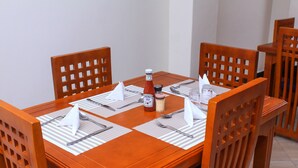 Una mesa de comedor de madera dispuesta con servilletas blancas, cubiertos y condimentos.