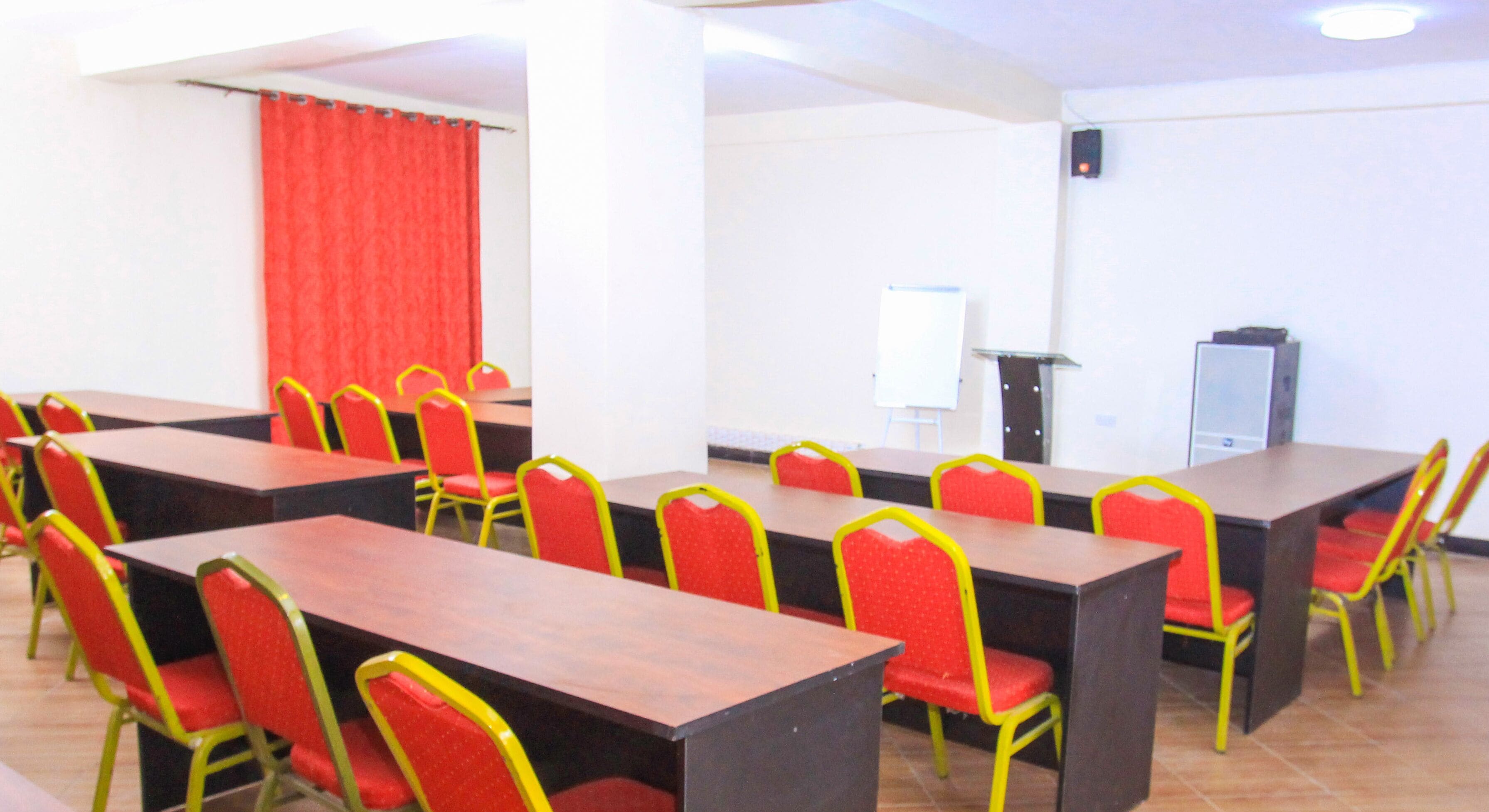 A conference room with multiple tables and chairs, a whiteboard, and a podium.