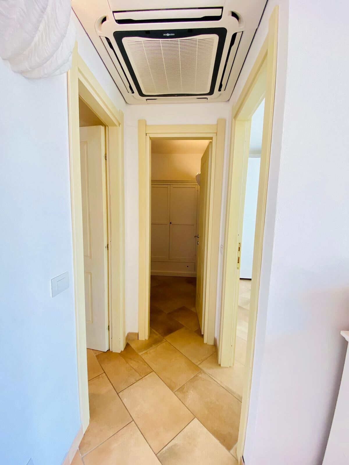 A hallway with a ceiling vent, a door on the left, and a door on the right leading to a room.