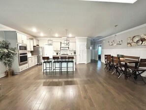 A modern kitchen with a central island, bar stools, and a dining area with a wooden table and chairs. - Spacious One Level Ranch Style Luxury Townhouse (Huntsville)
