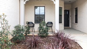 A covered porch with two chairs, a window, and a door.