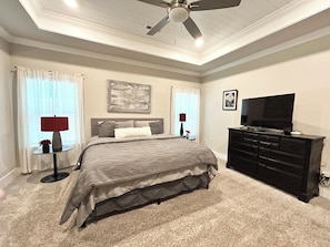 Quarto com cama, ventilador de teto, televisão, cômoda e duas luminárias.