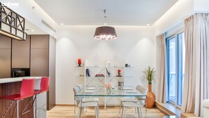A modern dining area with a glass table, white chairs, and a red bar counter. - bnbme | Al Murjan Tower | 2 BDR (Dubai)