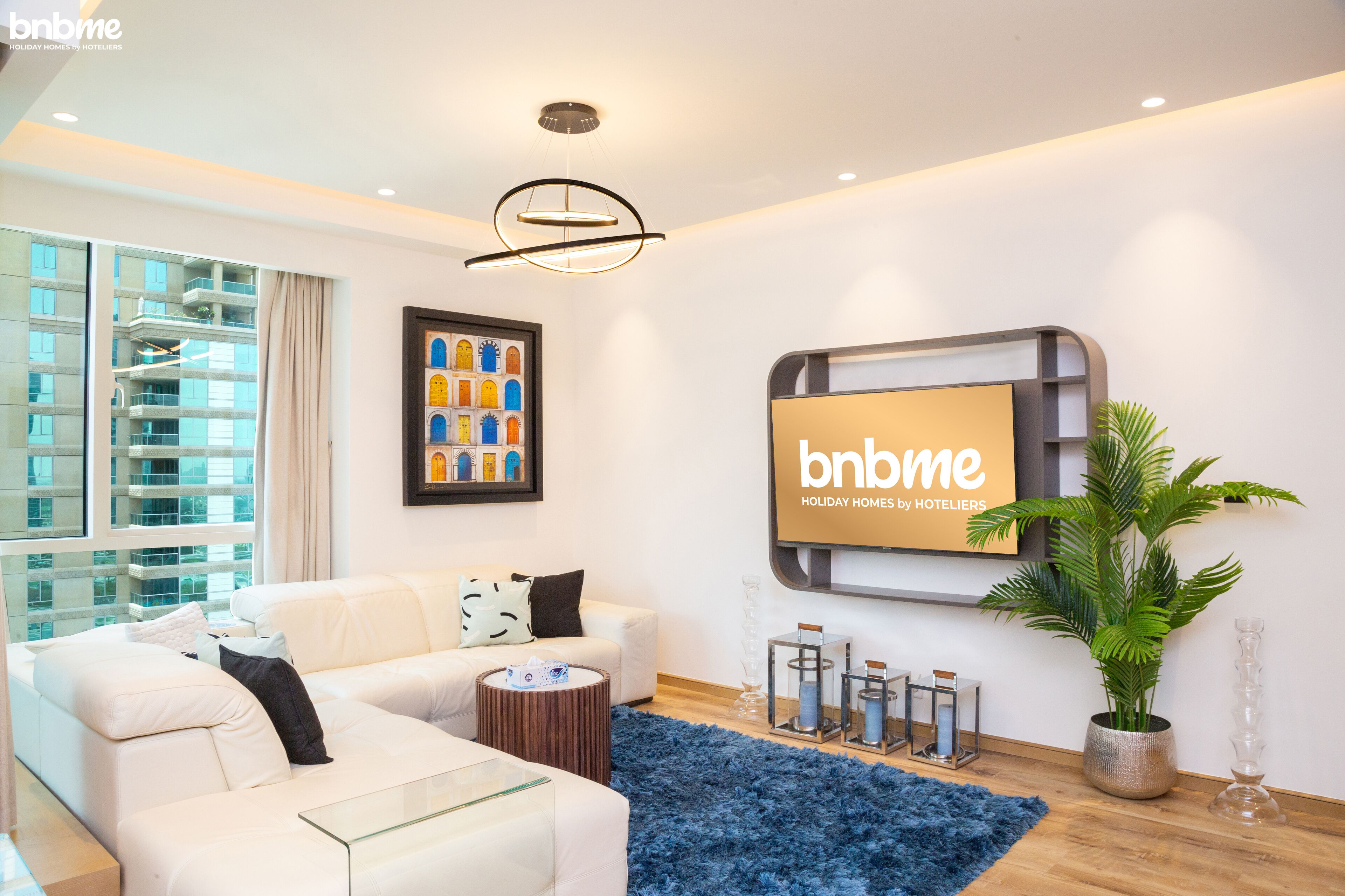 Ein modernes Wohnzimmer mit einem weißen Sofa, einem Glastisch, einem blauen Teppich, einer Topfpflanze und einem gerahmten Bild an der Wand.