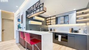 A modern kitchen with a central island, red bar stools, built-in appliances, and a wooden floor. - bnbme | Al Murjan Tower | 2 BDR (Dubai)