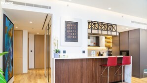 A modern reception area with a wooden counter, red bar stools, a potted plant, and a framed artwork on the wall. - bnbme | Al Murjan Tower | 2 BDR (Dubai)