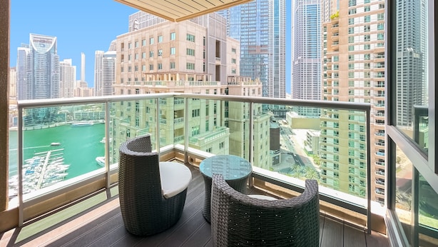 A balcony with wicker furniture and a view of a marina and cityscape. - bnbme | Al Murjan Tower | 2 BDR (Dubai)
