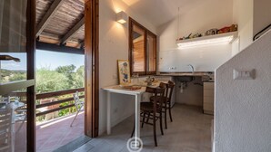A kitchen with a dining area, wooden ceiling, and a view of greenery outside. - Porto luna 24 - Selene (Villasimius)