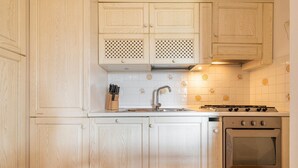 A kitchen with wooden cabinets, a stainless steel sink, and a gas stove. - Casa Perla - Domus de Maria (Domus De Maria)