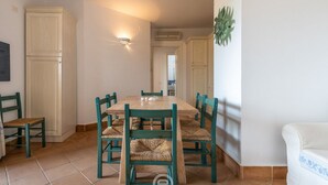 A dining area with a wooden table and chairs, a light fixture, and a view of the kitchen. - Casa Perla - Domus de Maria (Domus De Maria)