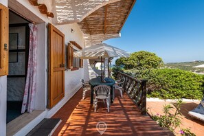 A terrace with a table and chairs, a wooden railing, and a view of greenery. - House Eleonora: Your Oasis of Sea and Relaxation in Cala Sapone (Sant'Antioco)