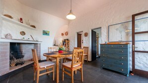 Ein Essbereich mit Kamin aus Ziegelsteinen, Holzstühlen, einem runden Tisch und einer blauen Kommode.