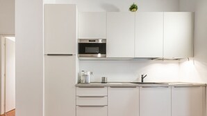 Uma cozinha moderna com armários brancos, forno embutido e geladeira de aço inoxidável.