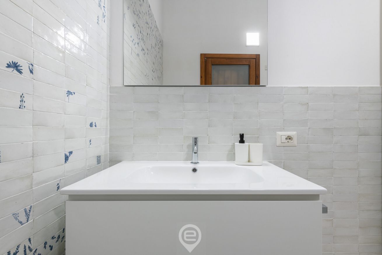 Un baño con un lavamanos blanco, un espejo y azulejos florales azules en la pared.