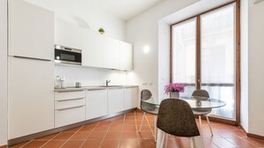 Cozinha moderna com armários brancos, micro-ondas e mesa de jantar de vidro com duas cadeiras.
