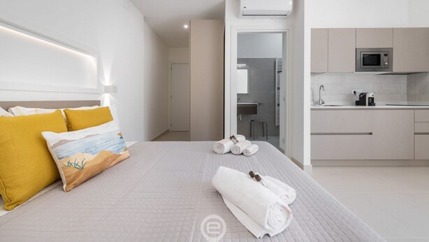 A modern hotel room with a bed, a small kitchenette, and a bathroom visible through an open door. - Al Parco Studios - Studio Botticelli (Cagliari)