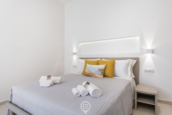 A neatly made bed with a headboard, two bedside tables, and a wall-mounted light fixture.